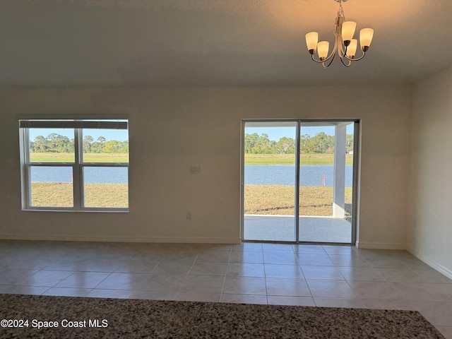 tiled spare room featuring a wealth of natural light, a water view, and a notable chandelier