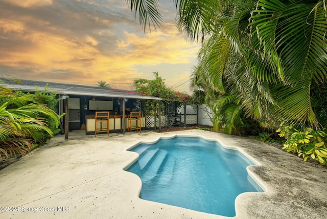 pool at dusk featuring exterior bar and a patio