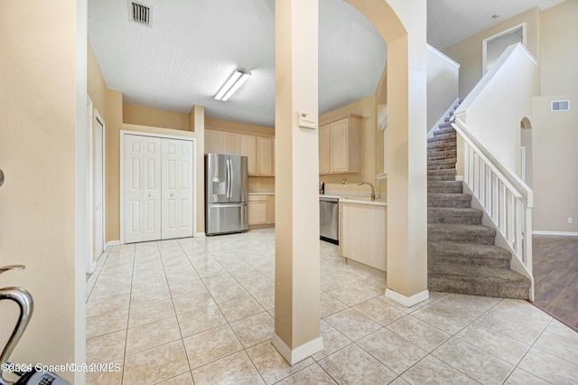 kitchen with sink, stainless steel appliances, a textured ceiling, light brown cabinetry, and light tile patterned floors