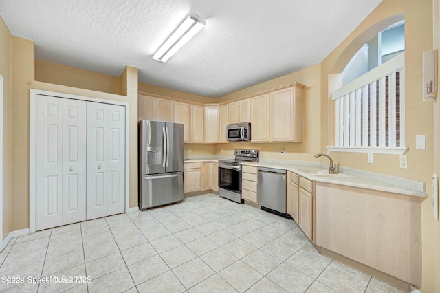 kitchen with sink, a textured ceiling, light brown cabinetry, appliances with stainless steel finishes, and light tile patterned flooring