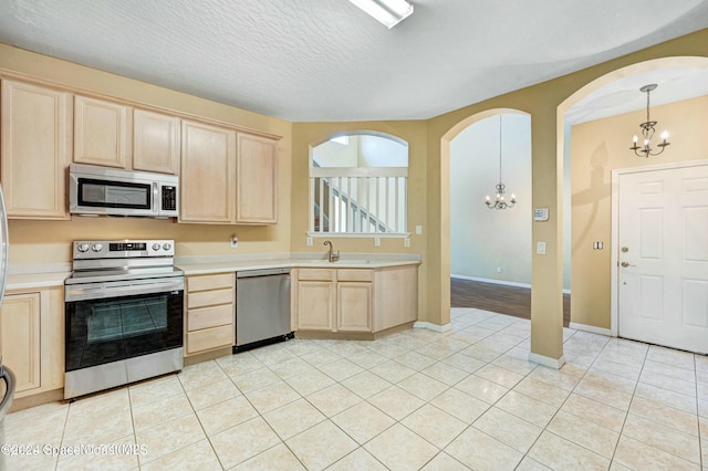 kitchen with light brown cabinets, an inviting chandelier, a textured ceiling, decorative light fixtures, and appliances with stainless steel finishes