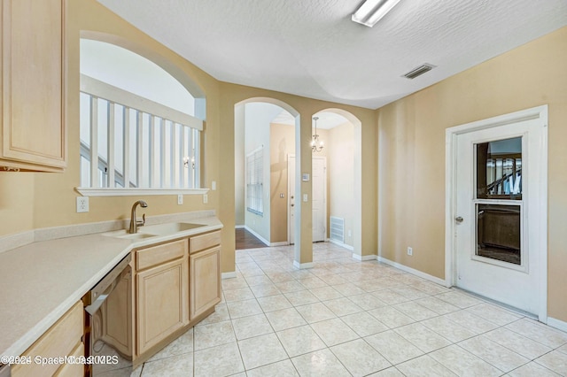 kitchen with light brown cabinetry, a textured ceiling, sink, light tile patterned floors, and dishwasher