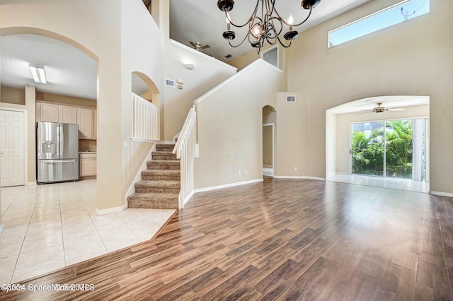 unfurnished living room with ceiling fan with notable chandelier, light wood-type flooring, a textured ceiling, and a high ceiling