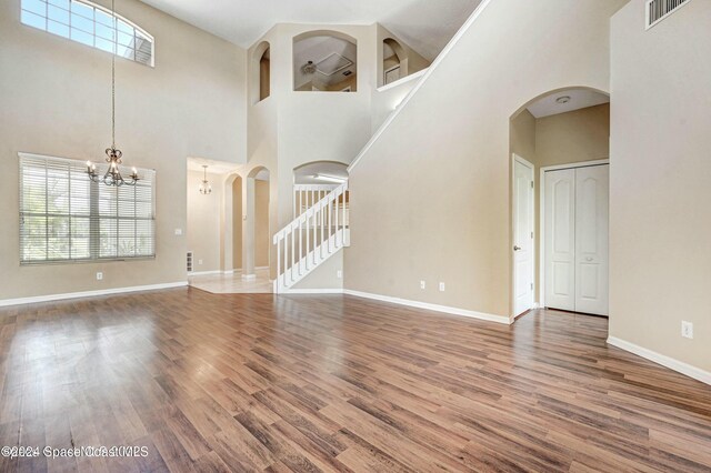 unfurnished living room featuring a chandelier, wood-type flooring, and a towering ceiling