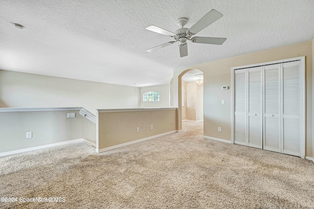 unfurnished bedroom with ceiling fan, a closet, light colored carpet, and a textured ceiling