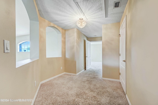 hallway with light colored carpet, a textured ceiling, and a chandelier