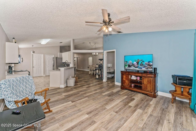 living room with vaulted ceiling, ceiling fan, a textured ceiling, and light hardwood / wood-style floors