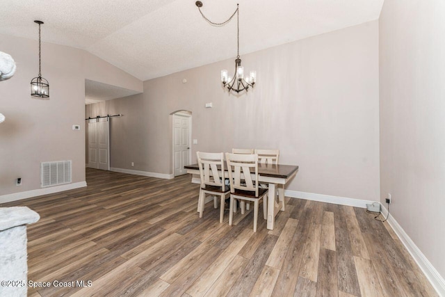 dining space featuring wood-type flooring, vaulted ceiling, a textured ceiling, a notable chandelier, and a barn door