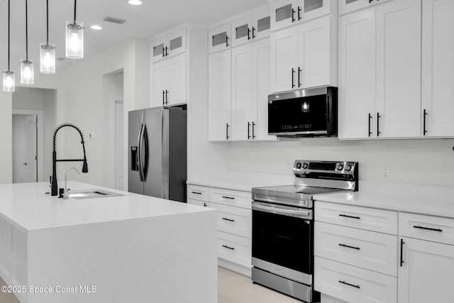 kitchen featuring appliances with stainless steel finishes, white cabinetry, sink, pendant lighting, and a center island with sink