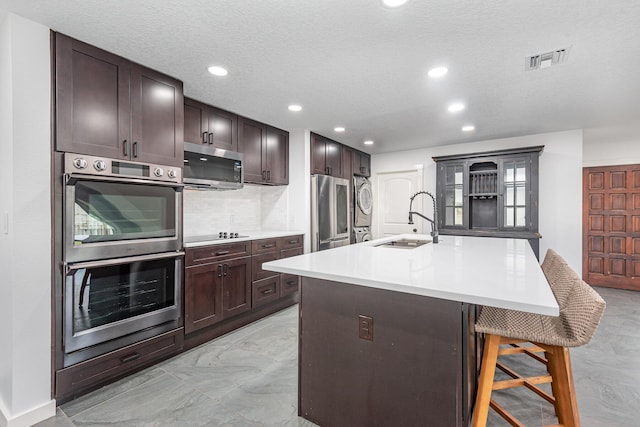 kitchen featuring sink, a textured ceiling, appliances with stainless steel finishes, an island with sink, and a kitchen bar