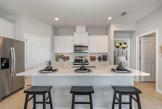 kitchen with white cabinets, appliances with stainless steel finishes, a kitchen bar, and a kitchen island with sink