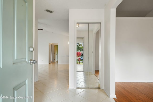 hall with light wood-type flooring, vaulted ceiling, and ornamental molding