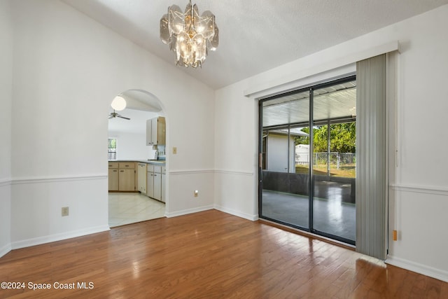 unfurnished room with a textured ceiling, light hardwood / wood-style flooring, ceiling fan with notable chandelier, and vaulted ceiling