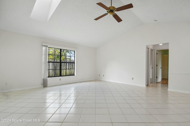 tiled empty room featuring ceiling fan, high vaulted ceiling, and a skylight