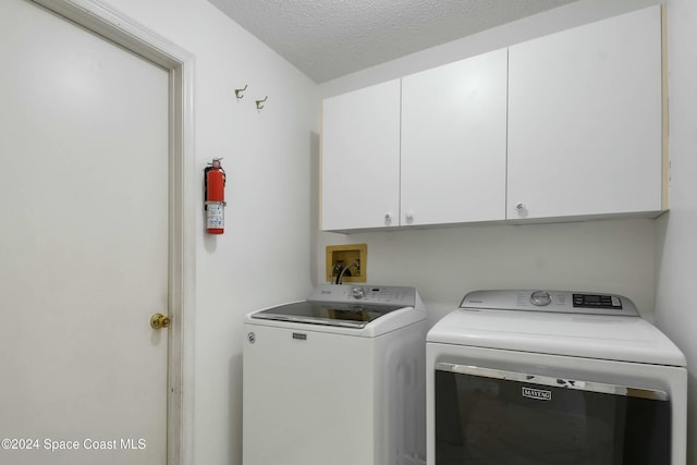 clothes washing area featuring cabinets, washer and dryer, and a textured ceiling