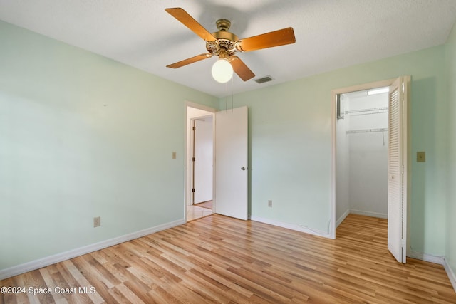 unfurnished bedroom with a textured ceiling, a closet, light hardwood / wood-style flooring, and ceiling fan