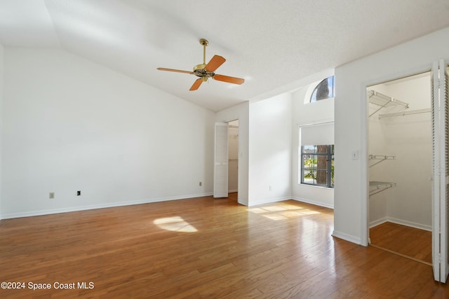 unfurnished bedroom featuring ceiling fan, wood-type flooring, vaulted ceiling, a walk in closet, and a closet