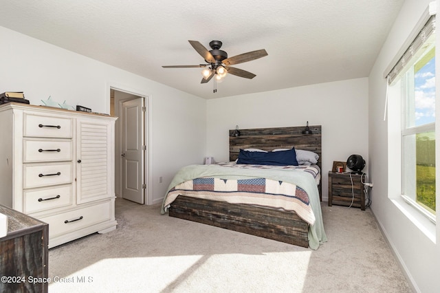 bedroom with ceiling fan, light colored carpet, and a textured ceiling