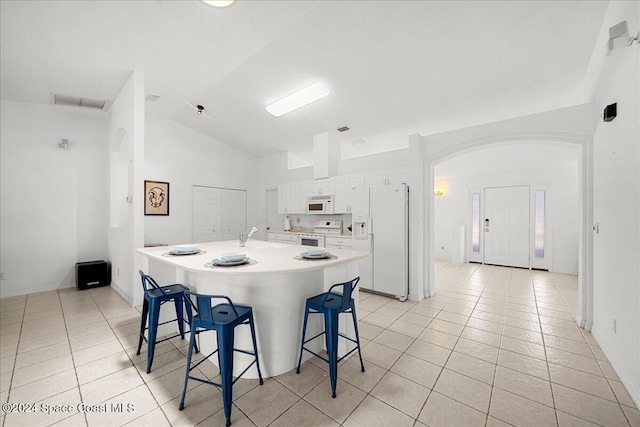 kitchen featuring lofted ceiling, white appliances, a center island with sink, white cabinetry, and a breakfast bar area