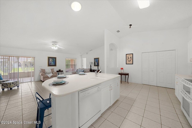 kitchen with white appliances, a kitchen island with sink, vaulted ceiling, ceiling fan, and white cabinetry