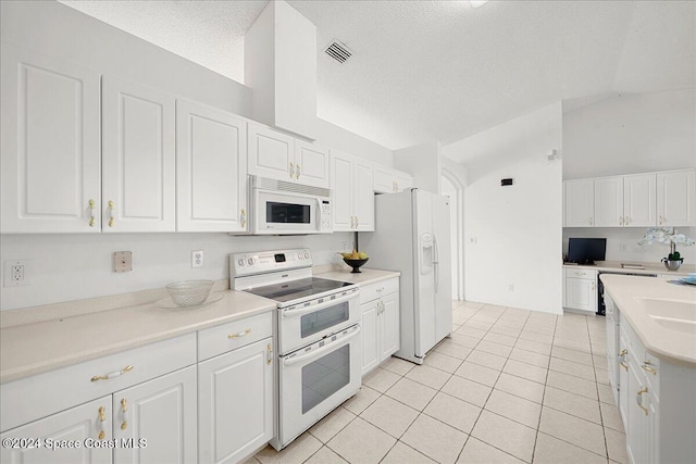 kitchen with a textured ceiling, white appliances, vaulted ceiling, white cabinetry, and light tile patterned flooring