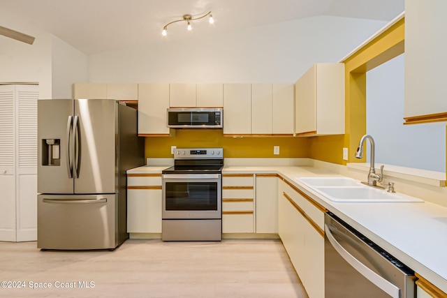 kitchen with stainless steel appliances, sink, cream cabinets, light hardwood / wood-style floors, and lofted ceiling