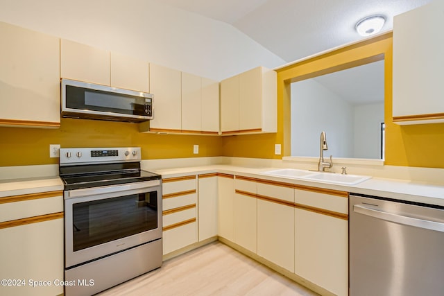 kitchen with sink, stainless steel appliances, cream cabinets, light hardwood / wood-style floors, and lofted ceiling