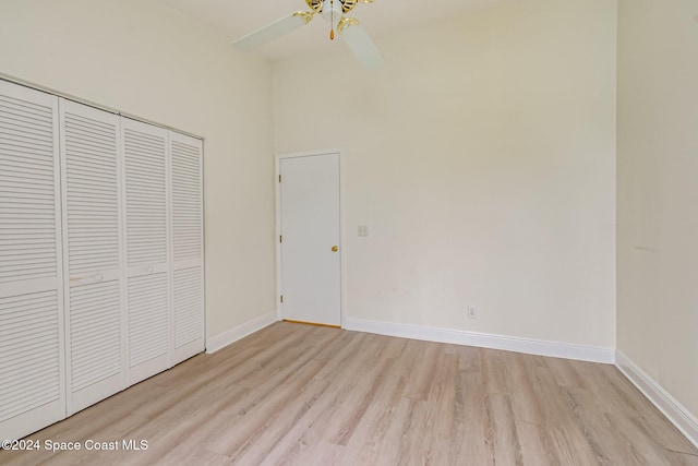 unfurnished bedroom with ceiling fan, light wood-type flooring, a towering ceiling, and a closet