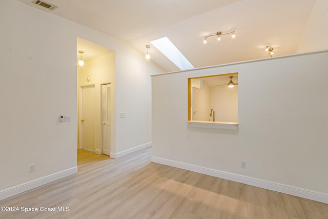 unfurnished room featuring sink, light wood-type flooring, ceiling fan, and vaulted ceiling with skylight