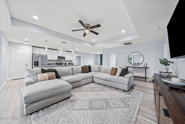 living room featuring ceiling fan, light wood-type flooring, and a tray ceiling