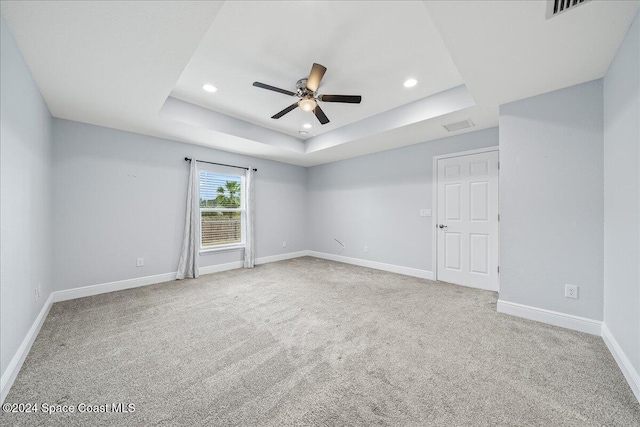 carpeted spare room featuring a raised ceiling and ceiling fan