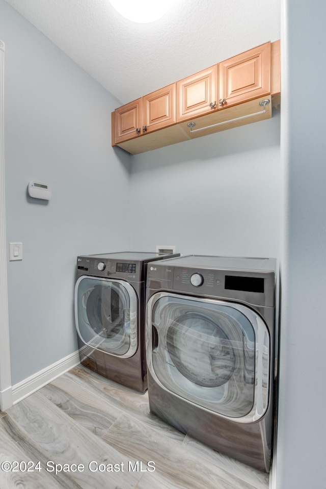 washroom with washer and clothes dryer, light hardwood / wood-style floors, cabinets, and a textured ceiling