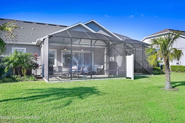 rear view of property with a lawn, glass enclosure, and ceiling fan