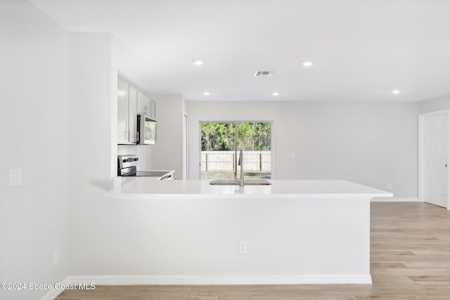 kitchen with kitchen peninsula, appliances with stainless steel finishes, sink, light hardwood / wood-style flooring, and white cabinets