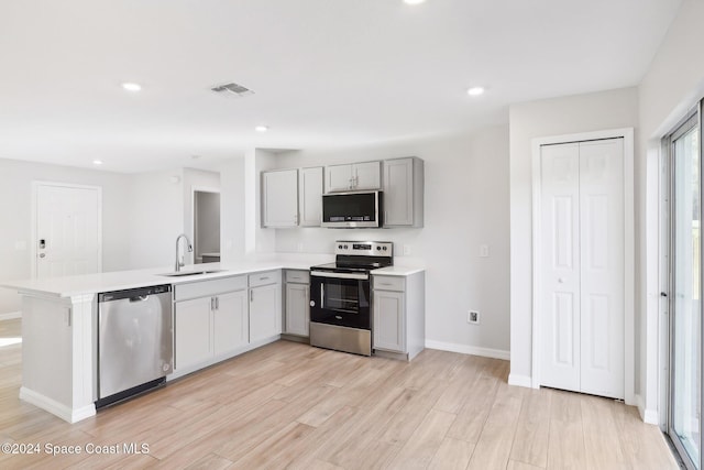 kitchen featuring kitchen peninsula, light wood-type flooring, gray cabinetry, stainless steel appliances, and sink