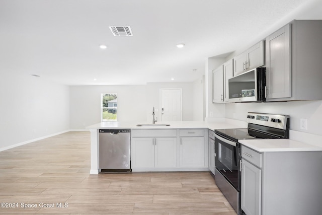 kitchen with gray cabinetry, sink, appliances with stainless steel finishes, light hardwood / wood-style floors, and kitchen peninsula