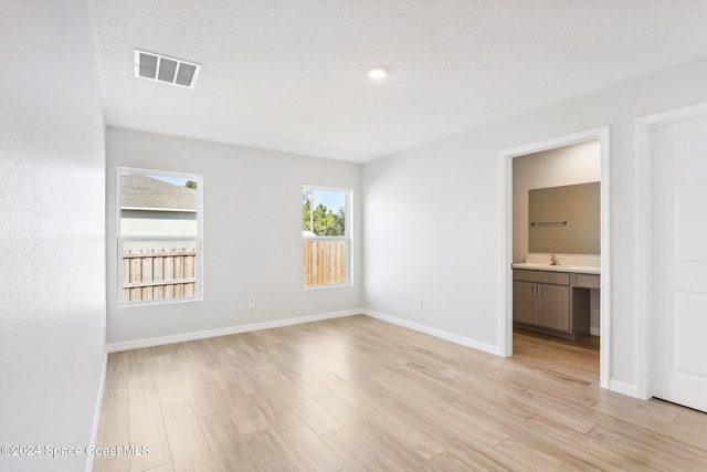 unfurnished bedroom with ensuite bathroom, sink, and light wood-type flooring