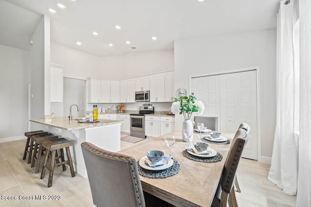 kitchen featuring a breakfast bar area, stainless steel appliances, light stone counters, sink, and white cabinetry