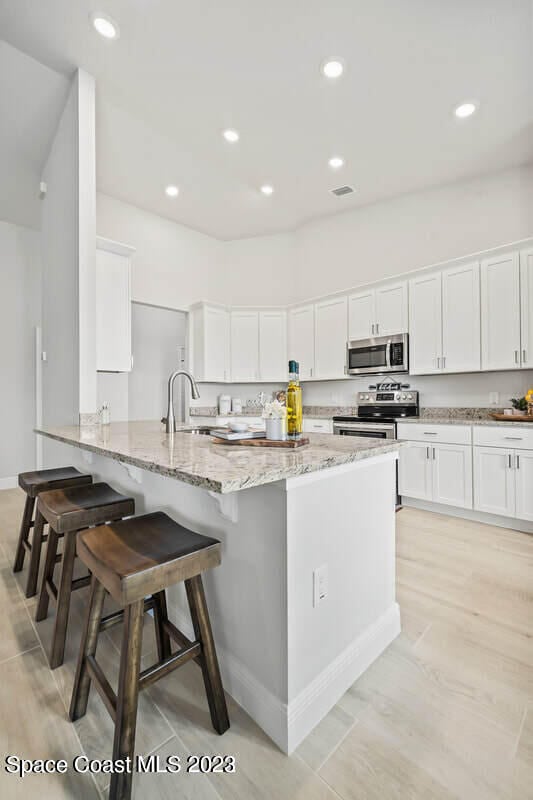 kitchen with light stone counters, kitchen peninsula, stainless steel appliances, white cabinetry, and a kitchen breakfast bar