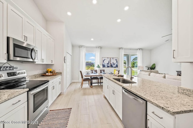 kitchen with sink, white cabinetry, light stone counters, light hardwood / wood-style flooring, and appliances with stainless steel finishes