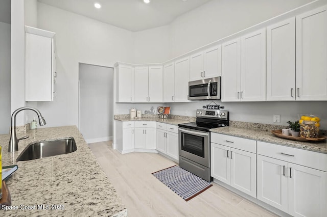 kitchen featuring light stone counters, light wood-type flooring, white cabinetry, appliances with stainless steel finishes, and sink