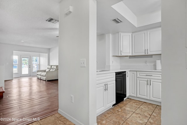 kitchen with black dishwasher, white cabinets, a textured ceiling, and light wood-type flooring