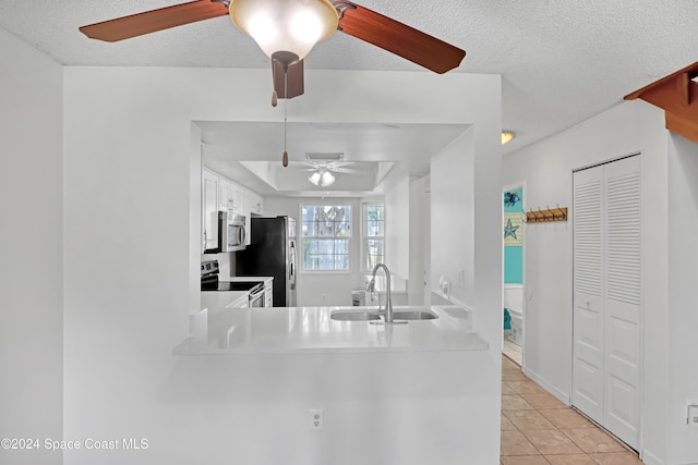 kitchen with kitchen peninsula, a textured ceiling, stainless steel appliances, sink, and light tile patterned floors