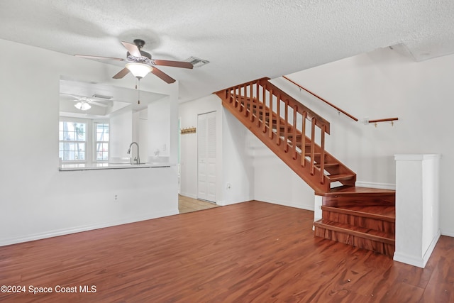 unfurnished living room featuring hardwood / wood-style flooring, ceiling fan, sink, and a textured ceiling