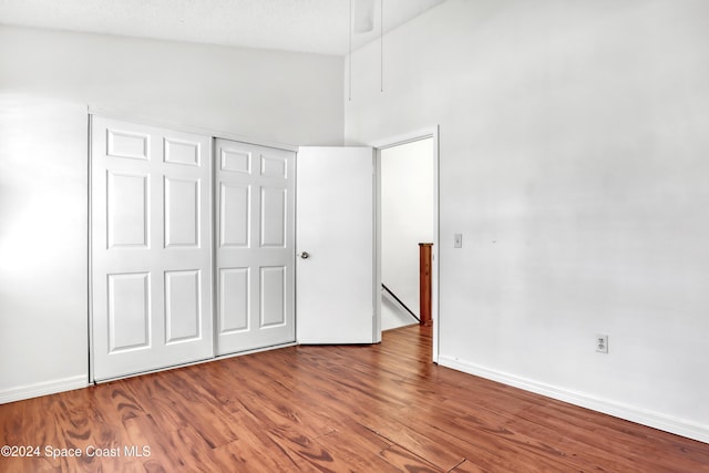 unfurnished bedroom featuring hardwood / wood-style floors, high vaulted ceiling, ceiling fan, a textured ceiling, and a closet