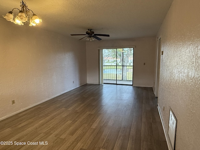 spare room featuring ceiling fan with notable chandelier, dark wood-type flooring, and a textured ceiling