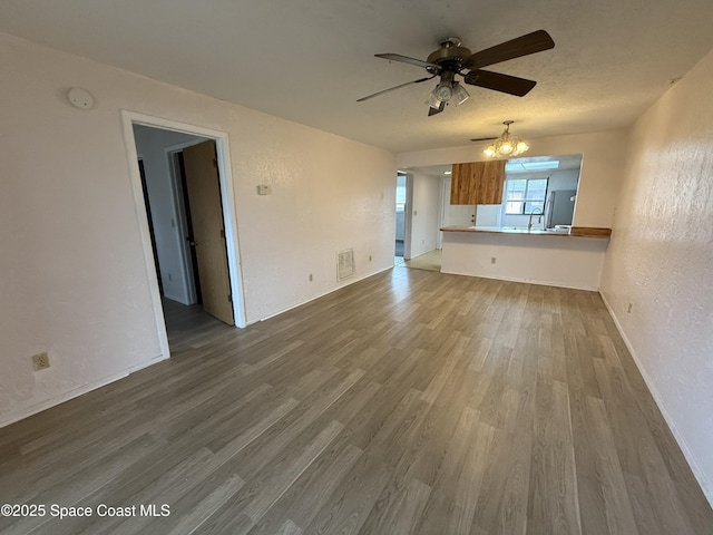 unfurnished living room featuring dark hardwood / wood-style floors, ceiling fan with notable chandelier, and a textured ceiling