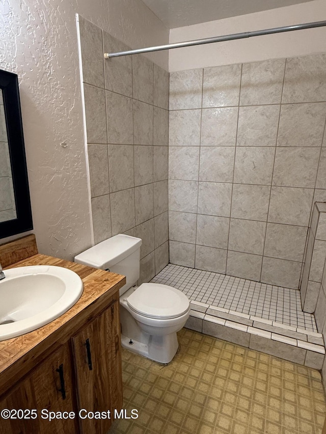 bathroom with vanity, a tile shower, and toilet