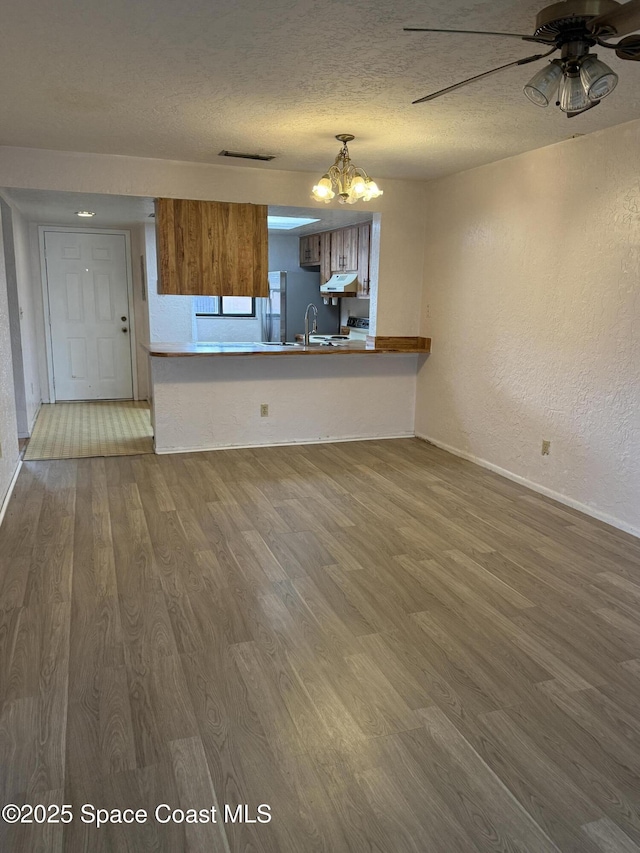 unfurnished living room with wood-type flooring, sink, ceiling fan with notable chandelier, and a textured ceiling