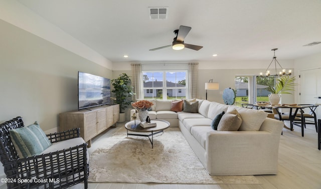 living room featuring ceiling fan with notable chandelier and light wood-type flooring